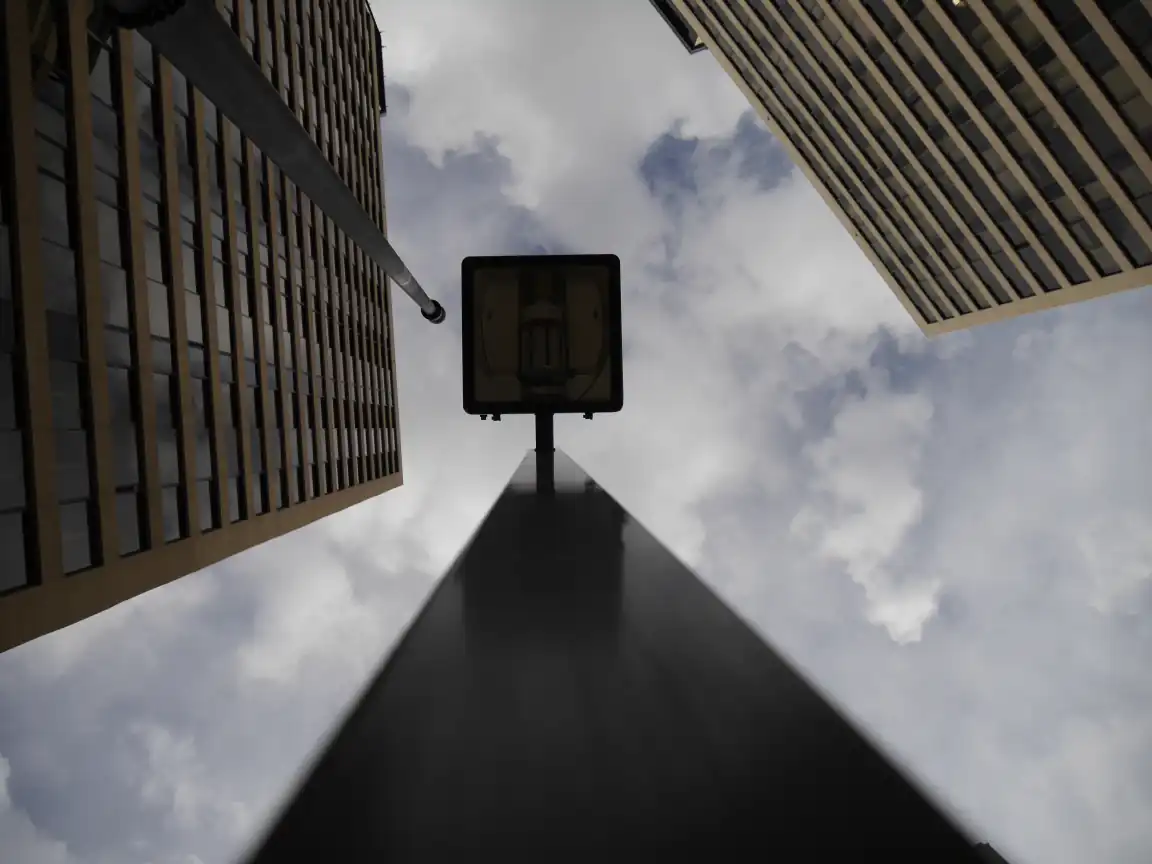 A streetlight viewed from underneath, with a flagpole and two buildings towering to the side